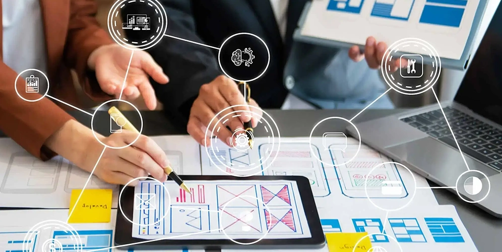 Designers planning UI/UX layouts on tablets and paper prototypes for a web application development project